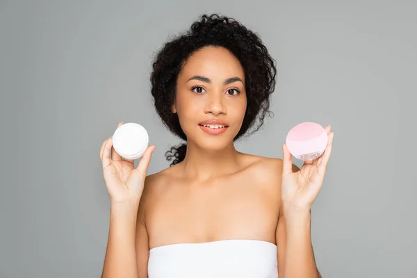 Mujer afroamericana joven sosteniendo limpiador de silicona y crema cosmética aislada en gris — Stock Photo