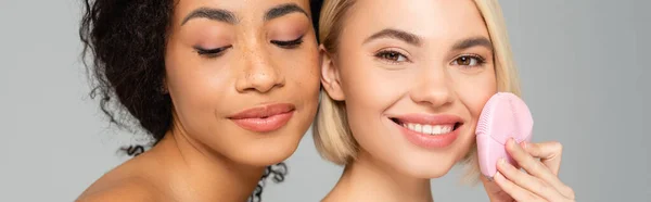 Mujeres jóvenes multiétnicas sosteniendo limpiador de silicona aislado en gris, pancarta — Stock Photo