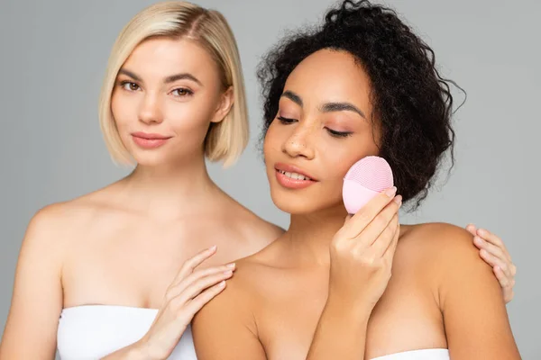 Femmes multiculturelles posant avec une brosse en silicone isolée sur gris — Photo de stock