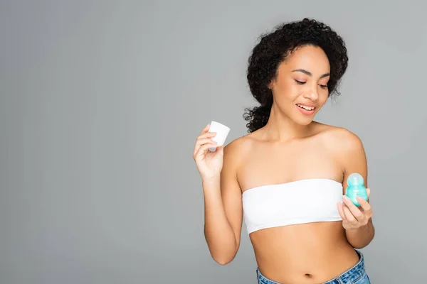 Sorridente donna afro-americana che tiene il deodorante isolato sul grigio — Foto stock