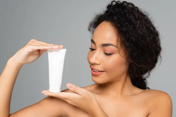 Femme afro-américaine souriante posant avec un tube de mousse nettoyante isolé sur gris — Photo de stock