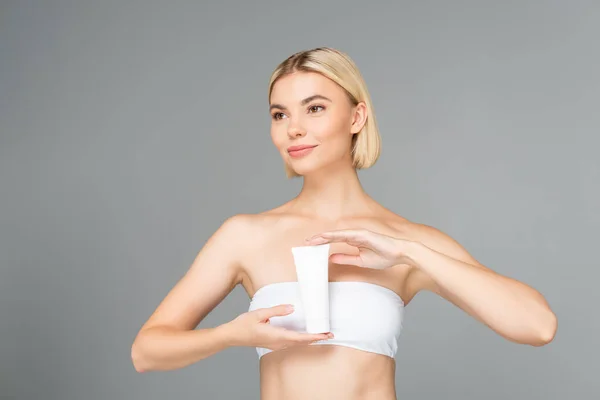 Donna bionda che distoglie lo sguardo mentre tiene il tubo con schiuma detergente isolata sul grigio — Foto stock