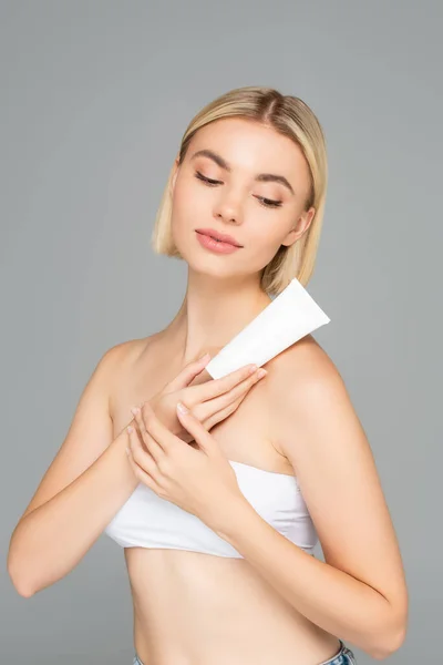 Femme blonde posant avec tube de lotion cosmétique isolé sur gris — Photo de stock