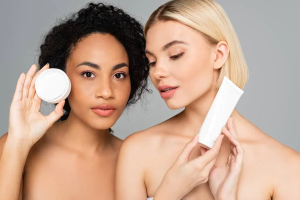 Mulheres multiétnicas com pele perfeita posando com creme cosmético isolado em cinza — Fotografia de Stock