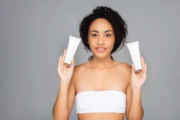 Femme afro-américaine tenant des tubes avec lotion hydratante isolée sur gris — Photo de stock