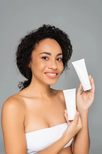 Young african american woman holding tubes with cleansing foam isolated on grey — Stock Photo