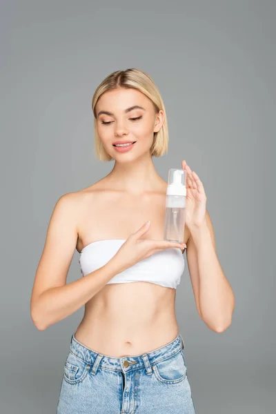 Smiling woman in white top holding cleansing foam isolated on grey — Stock Photo