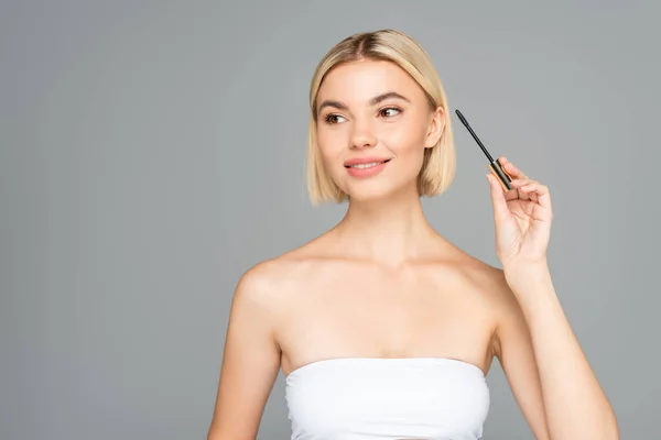 Donna sorridente che tiene applicatore per mascara isolato su grigio — Foto stock