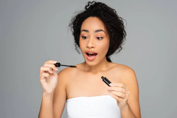 Aufgeregte Afroamerikanerin hält Mascara isoliert auf grau — Stockfoto