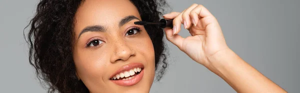 Retrato de mulher afro-americana aplicando rímel isolado em cinza, banner — Fotografia de Stock