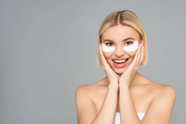 Femme souriante avec des patchs pour les yeux regardant la caméra isolée sur gris — Photo de stock