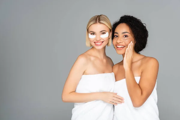 Positive multiethnic women in eye patches and towels isolated on grey — Stock Photo