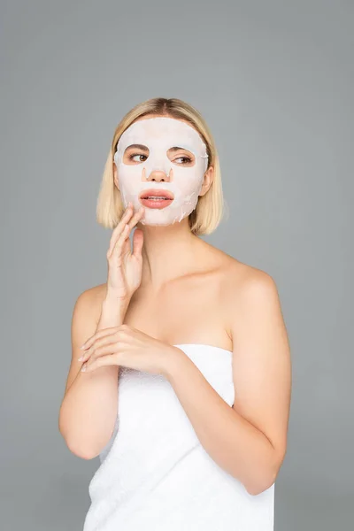 Young woman in towel and sheet mask on face isolated on grey — Stock Photo