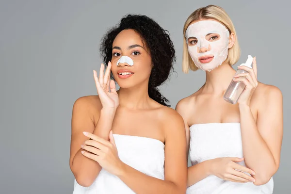 Lächelnde multikulturelle Frauen in Lakenmaske und Reinigungsstreifen, die Schaum isoliert auf Grau halten — Stockfoto