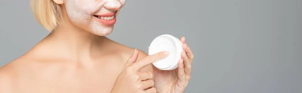 Vista ritagliata di donna sorridente con maschera facciale contenente crema cosmetica, banner isolato su grigio — Foto stock