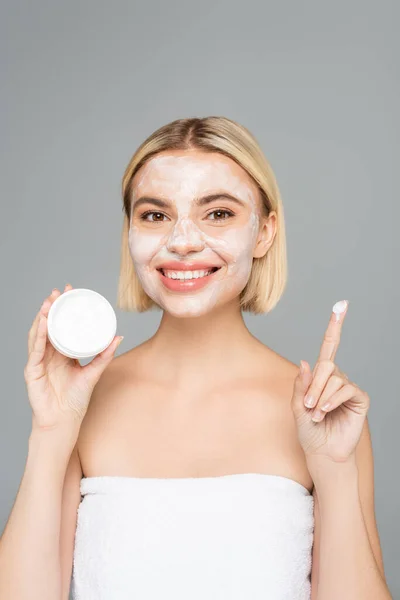 Blonde woman with facial mask holding cosmetic cream isolated on grey — Stock Photo