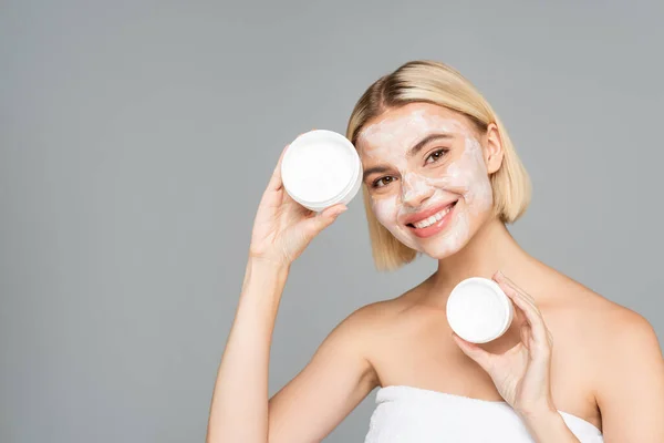 Happy woman in facial mask holding cosmetic cream isolated on grey — Stock Photo