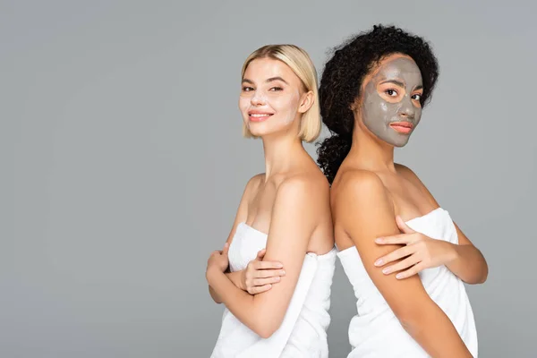 Mulheres multiculturais em máscaras faciais e toalhas olhando para câmera isolada em cinza — Fotografia de Stock