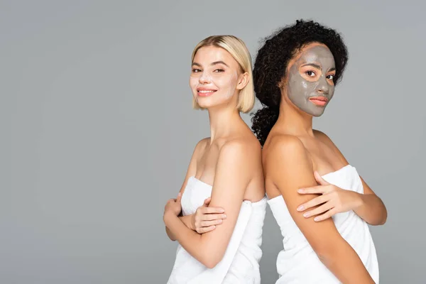 Mujeres multiculturales en máscaras faciales y toallas mirando a la cámara aislada en gris - foto de stock