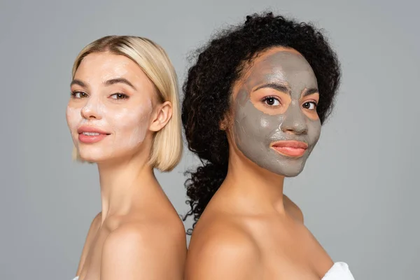 Multiethnic women in facial masks standing back to back isolated on grey — Stock Photo