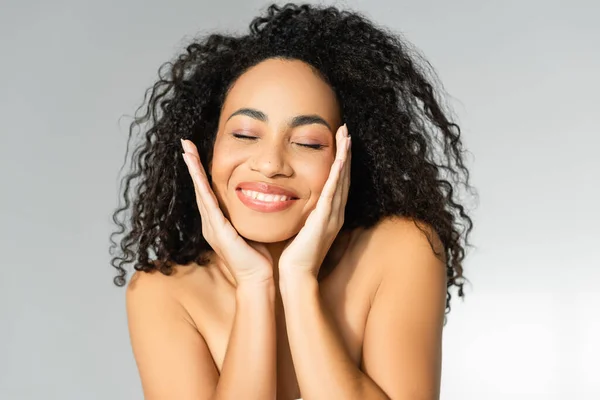 Joven mujer afroamericana con la piel perfecta sonriendo con los ojos cerrados aislados en gris - foto de stock