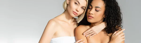 Blonde woman embracing african american woman on grey background, banner — Stock Photo