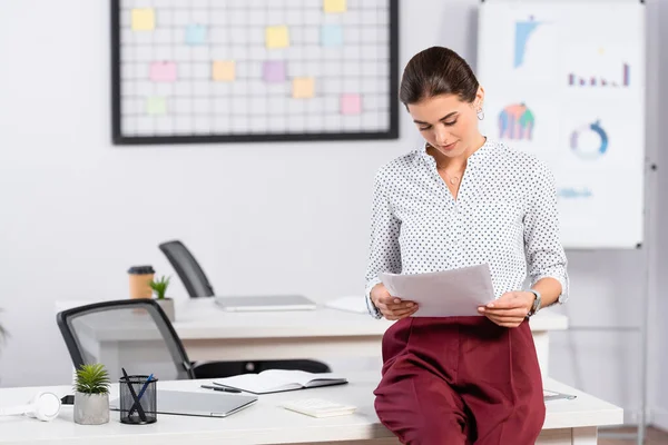 Geschäftsfrau stützt sich auf Schreibtisch und hält Dokumente im Büro — Stockfoto