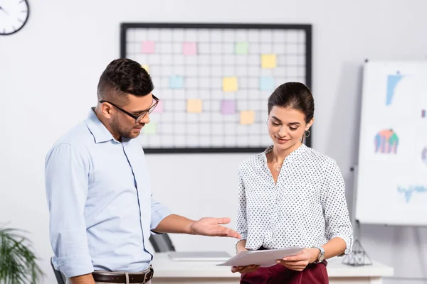 Hombre de negocios en gafas apuntando con la mano a documentos en manos de una mujer de negocios sonriente — Stock Photo