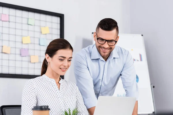 Cheerful business people looking at laptop in office with blurred foreground — Stock Photo