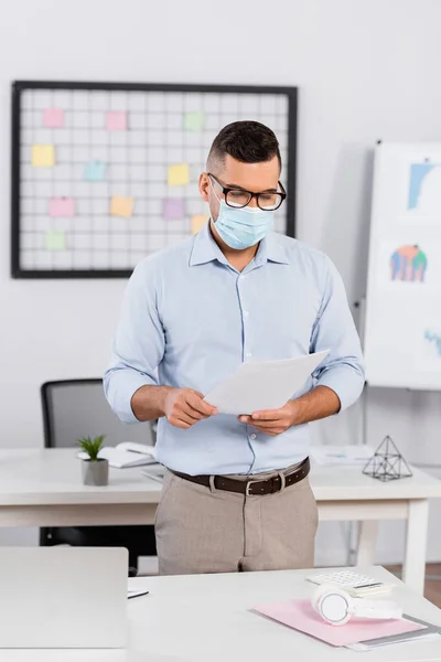 Hombre de negocios en máscara médica y gafas mirando documentos - foto de stock