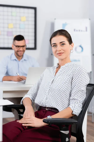 Businesswoman looking at camera near businessman on blurred background — Stock Photo