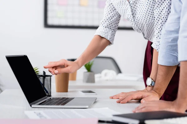 Vista recortada de la mujer de negocios apuntando con el dedo a la computadora portátil con pantalla en blanco en el escritorio - foto de stock