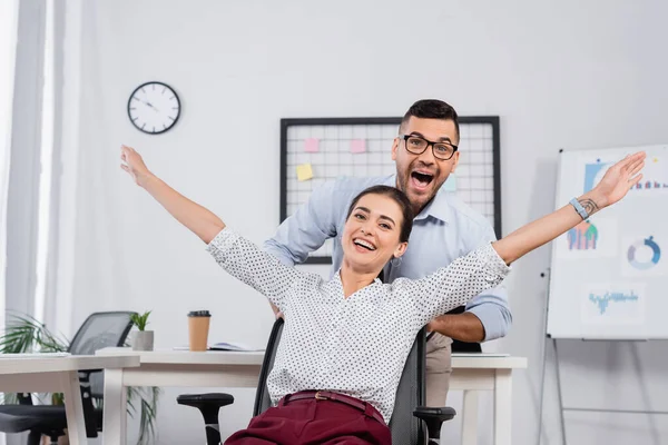 Homme d'affaires excité derrière femme d'affaires étonnée avec les mains tendues sur la chaise — Photo de stock