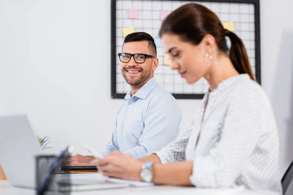 Feliz hombre de negocios en gafas mirando a la mujer de negocios en primer plano borrosa - foto de stock