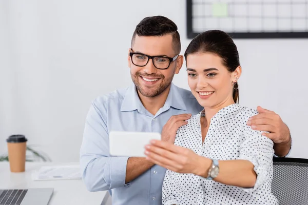 Cheerful businesswoman taking selfie with coworker in glasses — Stock Photo