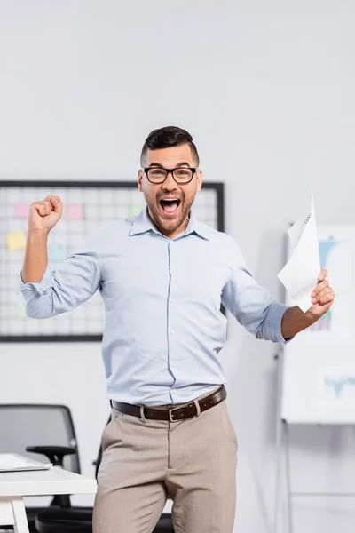 Empresário animado em óculos segurando documento no escritório — Fotografia de Stock