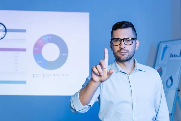 Hombre de negocios en gafas apuntando con el dedo cerca de gráficos y gráficos - foto de stock