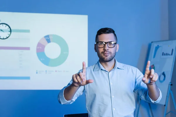 Hombre de negocios en gafas apuntando con los dedos cerca de gráficos y gráficos - foto de stock