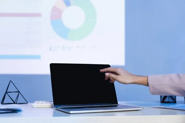 Vista recortada de la mujer de negocios apuntando con el dedo a la computadora portátil con pantalla en blanco en el escritorio - foto de stock