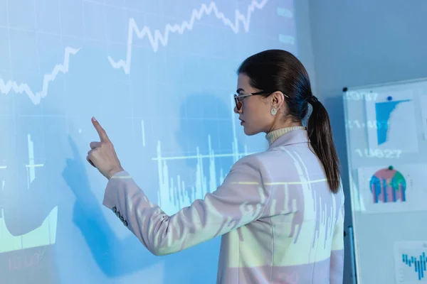 Mujer de negocios en gafas y apuntando con el dedo a gráficos digitales - foto de stock