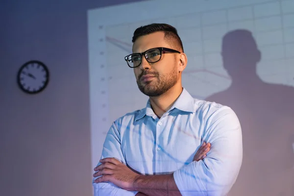 Hombre de negocios en gafas de pie con los brazos cruzados en la oficina - foto de stock