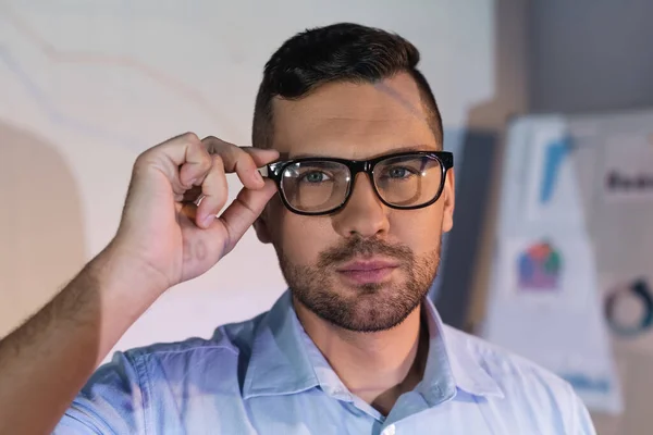 Businessman adjusting glasses and looking at camera — Stock Photo