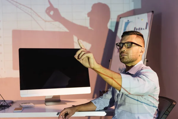 Businessman in glasses pointing with finger near computer monitor with blank screen — Stock Photo