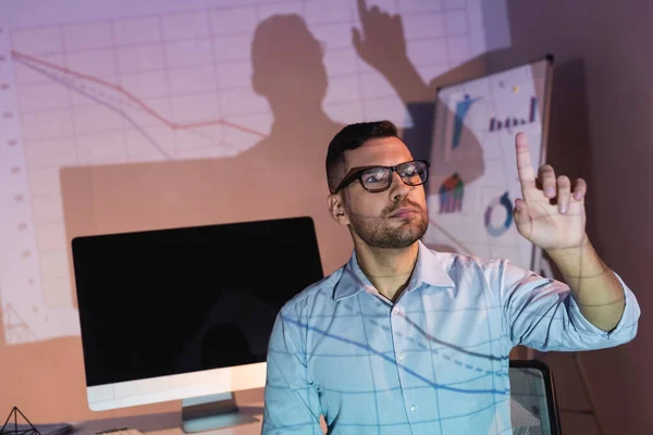 Hombre de negocios en gafas apuntando con el dedo cerca del monitor de la computadora con pantalla en blanco en la oficina - foto de stock