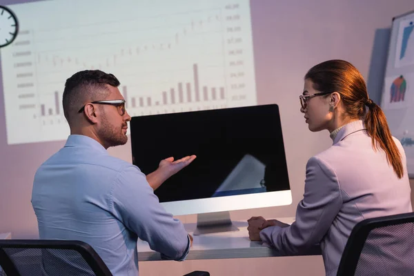 Geschäftsmann mit Brille zeigt mit der Hand auf Computermonitor mit leerem Bildschirm in der Nähe von Mitarbeiter im Büro — Stockfoto