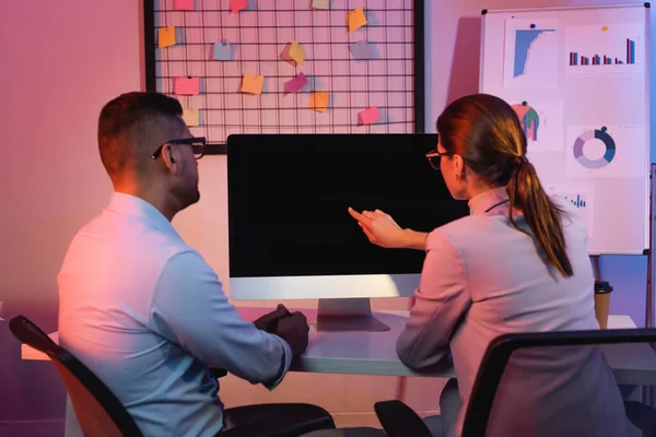Empresária apontando com o dedo para monitor de computador com tela em branco perto colega de trabalho no escritório — Fotografia de Stock