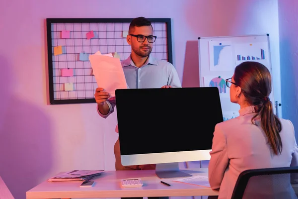 Geschäftsfrau sitzt neben Computermonitor mit leerem Bildschirm und schaut Mitarbeiter mit Dokumenten an — Stockfoto