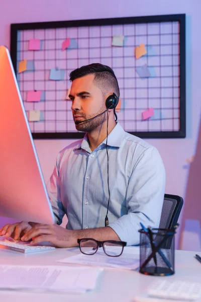 Operator in headset typing on computer keyboard and looking at monitor — Stock Photo