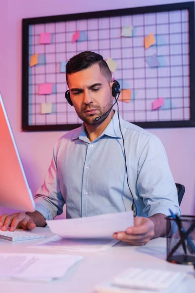 Operator in headset looking at paper near computer monitor — Stock Photo