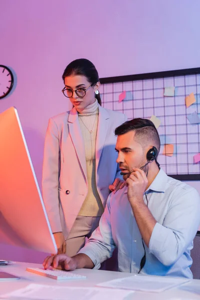 Operator in headset looking at computer monitor near businesswoman — Stock Photo